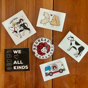
                  
                    photo of five stickers on table. from top right, going clockwise, RHC curds on cow, macaroni and cheese holding hands, solo cow, RHC cheese van, we heart all kind, RHC logo
                  
                